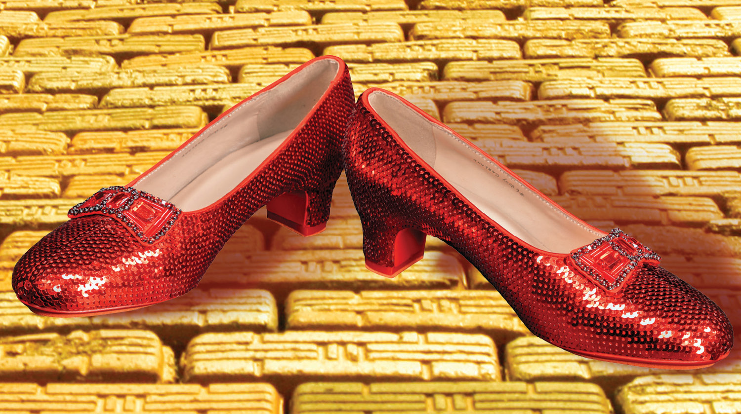 Image of a pair of red sequined shoes with rhinestone bows and 1-inch heels. The shoes are turned out at the toes and sit on a yellow brick road. 