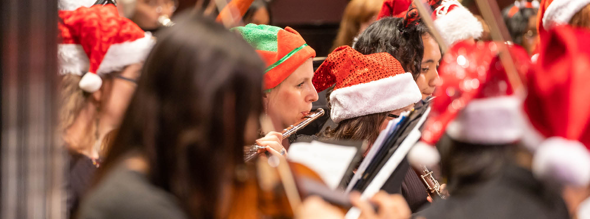Image of a section of The Rose Orchestra playing their instruments dressed in Santa hats and elves hats. 