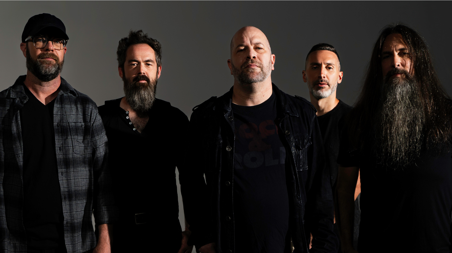 Five men from a rock band standing together against a dark background, wearing black and serious expressions.