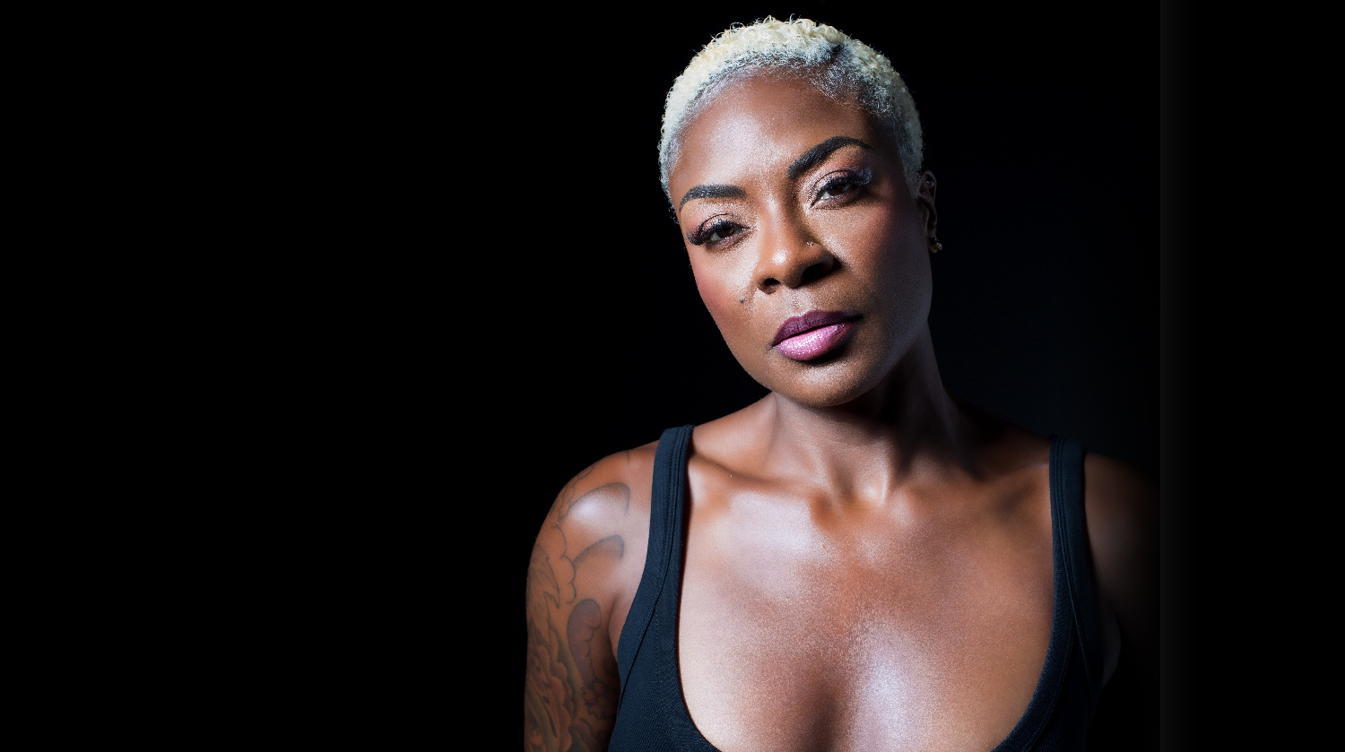 "Close-up portrait of a woman with a short blonde haircut, wearing a black tank top, looking confidently into the camera."