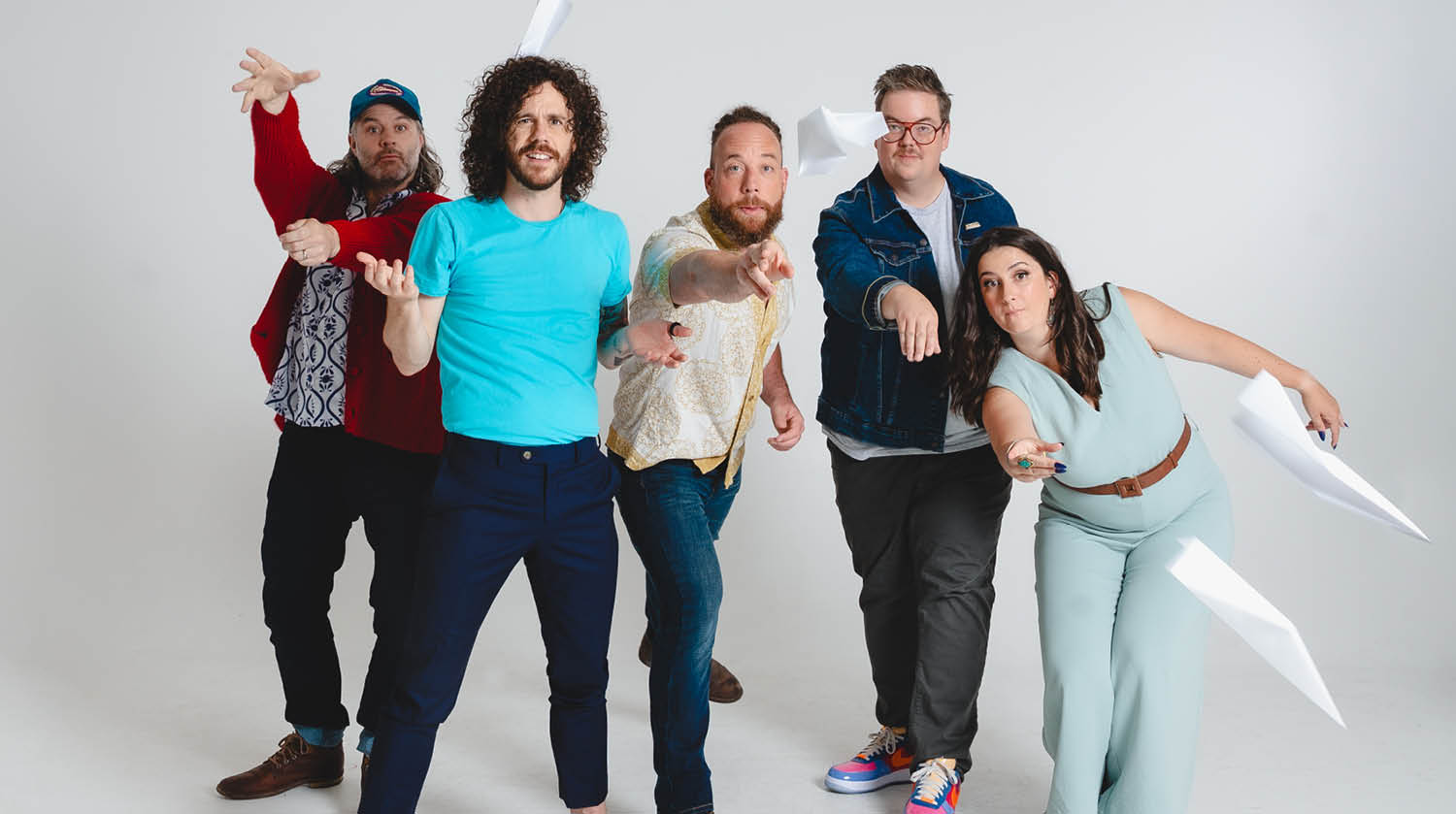 Five people in playful poses with paper airplanes against a white background, one in red pointing, one in blue leaning forward, another in yellow pointing, one in denim gesturing, and one in teal crouching with a plane.