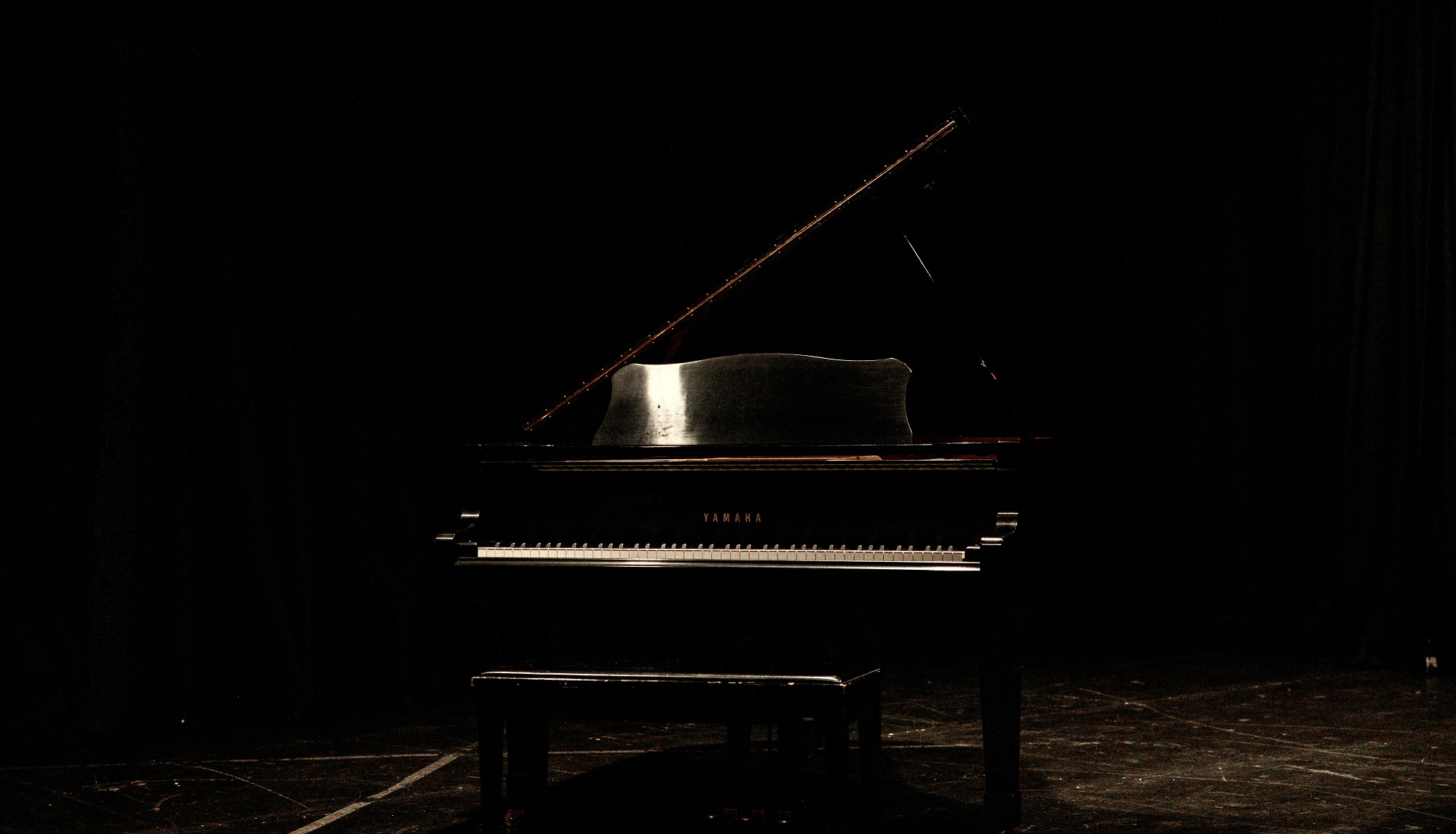 Black grand piano with lid propped open on a black stage