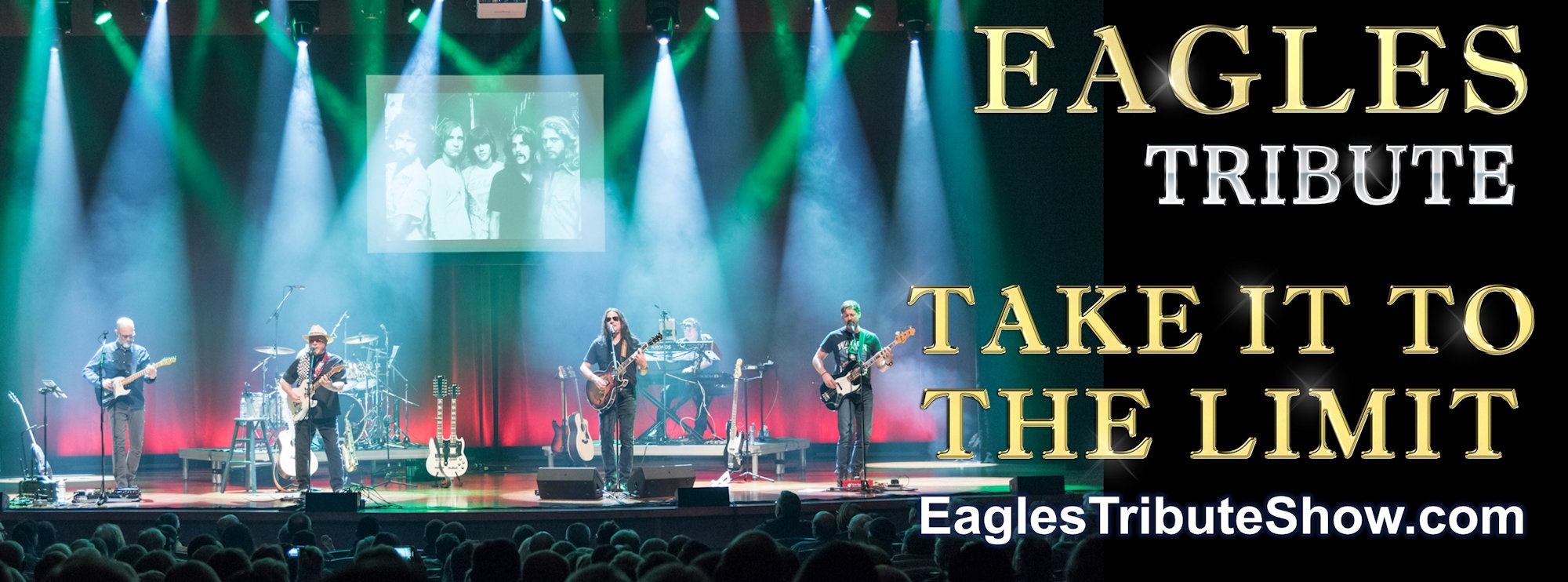 live performance image with green and blue lighting.  Across the front of the stage, four men playing guitars and singing (3 Caucasian males and 1 indigenous male). Towards the left back of the stage is the drummer, and the right back is our Ukrainian keyboard player. In middle back of stage is projection screen is a picture of the Eagles.  