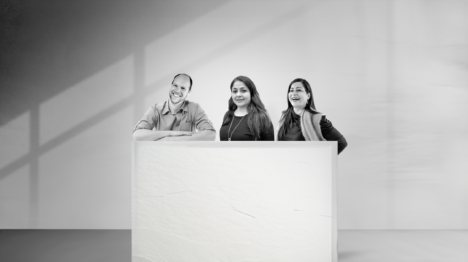 Three smiling professionals standing behind a presentation podium in a black and white office setting.
